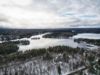 Aerial drone over Trafalgar Bay and Gaunt Bay in rural cottage country Bala, located in the Muskoka Lakes region of Ontario, Canada. Evergreen trees and snow during a cold winter day.