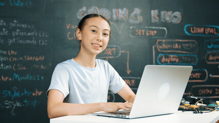 Smart girl programing system by using laptop at blackboard. Highschool student writing engineering code or prompt while looking at camera at STEM technology class. Creative education. Edification.