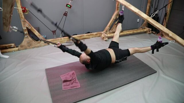 A bald man performs a swinging exercise with a weight on a pendant