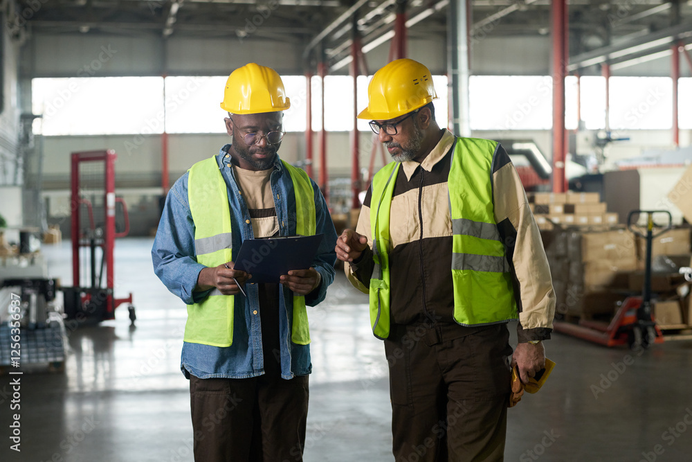 Poster two intercultural workers of modern factory or plant looking at document in folder held by one of th