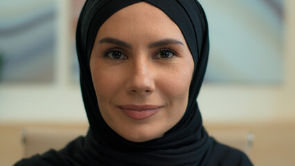 Close up face serious calm Arabian ethnic woman muslim islamic girl wearing hijab islam traditional middle eastern clothes female businesswoman business lady boss employer looking at camera at office