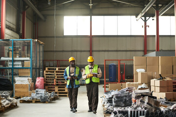 Young and mature male workers of large warehouse discussing quality of new equipment while walking...