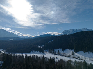 View from the drone of high mountains range, white peaks, green fir forestes and snow