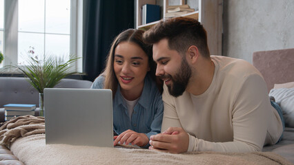 Caucasian family couple in love woman wife and man husband shopping online with laptop computer on cozy bed smiling boyfriend and girlfriend booking tickets buy internet order e-commerce talk together