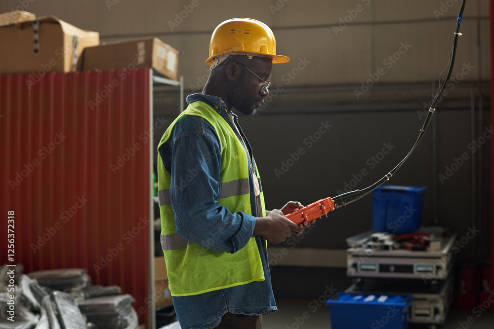 Poster Side view of African American factory worker pressing buttons on control pad while working with industrial equipment in warehouse