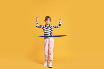 Cute little girl exercising with hula hoop on orange background