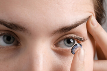 Woman putting in blue color contact lens, closeup