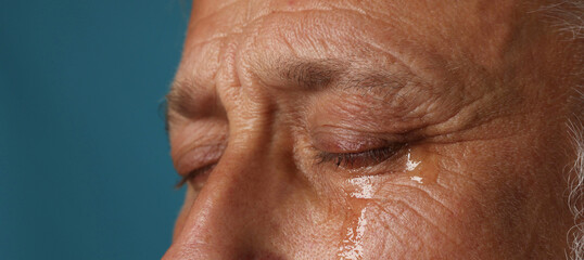 Sad senior man crying on blue background, closeup