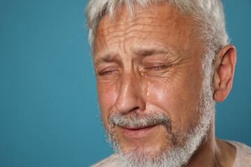Sad senior man crying on light blue background, closeup. Space for text