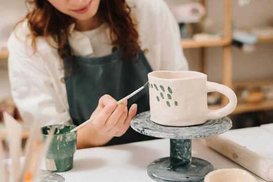 Process of designing cup with a traditional pattern in pottery art studio. Artisan stamps decorative symbols on the dry clay of the cup.