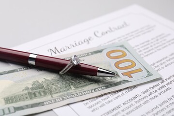 Marriage contract, pen with ring and dollar bill on grey table, closeup