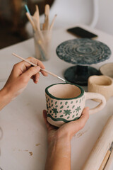 Design earthenware cup with a traditional pattern. Artist is making decoration on the clay ceramic mug after oven firing.