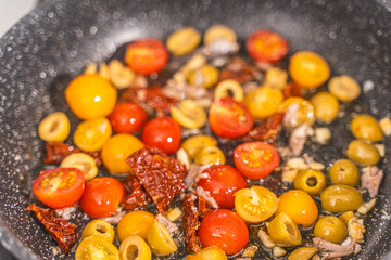 Cook the spaghetti Puttanesca, fry the tomatoes, anchovies, olives and capers with garlic in a pan. Close-up.