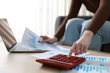 Budget. Woman with paperwork and calculator at wooden desk indoors, closeup