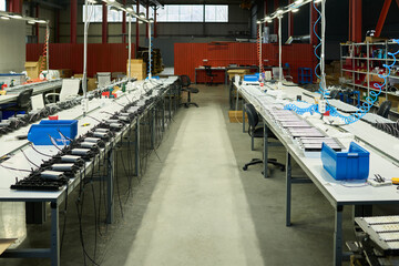 Long aisle between tables with electric equipment prepared for producing new items in spacious workshop of modern factory
