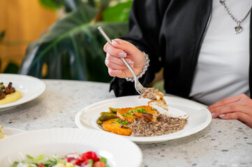 A close-up of a hand holding a fork, ready to eat a gourmet dish featuring tender meat, creamy sauce, and garnishes, with a modern dining setting in the background.