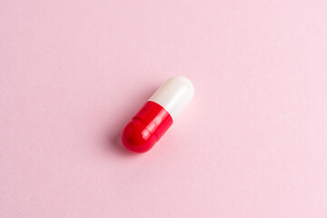 White-red pill capsule on a pink background. Minimal pharmacy concept. Flat lay.