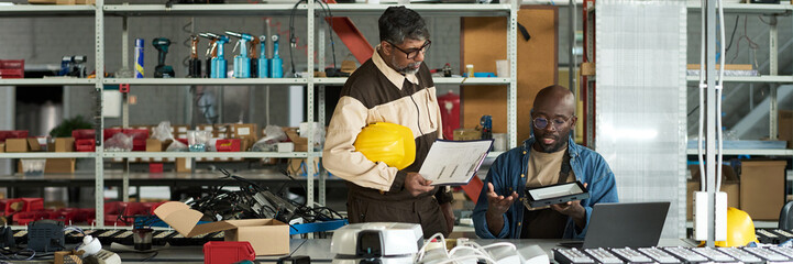 Header of young male engineer with lamp and his boss with working documents discussing principles...
