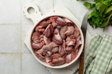 Poultry Offal on a white table. Cooking chicken gizzards, raw, uncooked meat, vegetable ingredients. Top view.