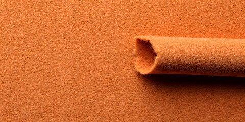 Obraz premium Close-up of orange felt fabric, showcasing its soft texture and vibrant color. Partially rolled up, it evokes creativity and warmth. Ideal for crafts and design projects.