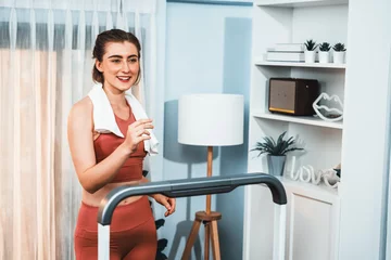 Gordijnen Athletic and sporty woman running on treadmill running machine during home body workout exercise session for fit physique and healthy sport lifestyle at home. Gaiety home exercise workout training. © InfiniteFlow
