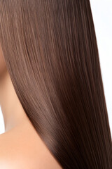 Fototapeta premium Close-up of long, straight, shiny brunette hair cascading over a shoulder, showcasing its smooth texture and healthy appearance against a bright background.