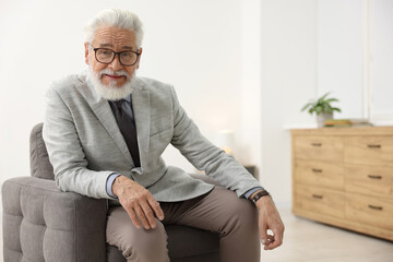Portrait of handsome bearded man in armchair indoors, space for text