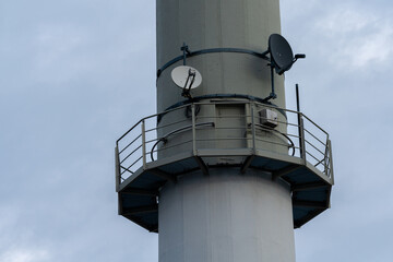 Satellite dish mounted on tall communication tower against cloudy sky