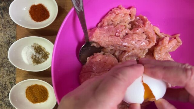 Adding raw chicken egg, salt, black pepper and other spices to raw minced chicken. The process of making chicken frikadelles. Top view.