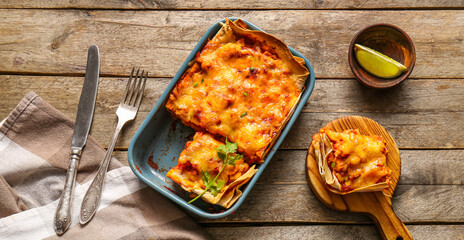 Composition with tasty enchilada and cutlery on wooden background