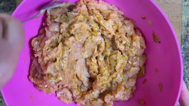 Mixing raw minced chicken and fried onions with a spoon in a bowl. The process of making chicken frikadelles. Top view.