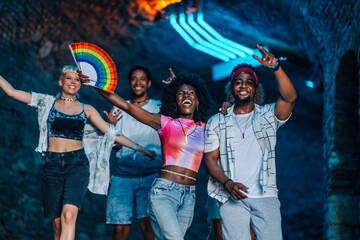 Friends celebrating at music festival with rainbow fan, dancing and enjoying youthful energy