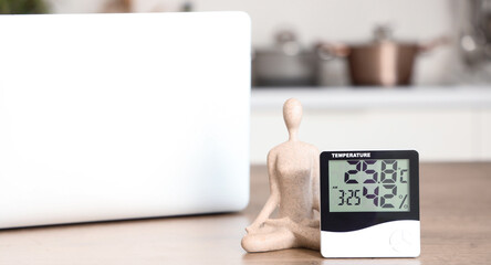 Digital hygrometer with statuette and laptop on table in kitchen, closeup