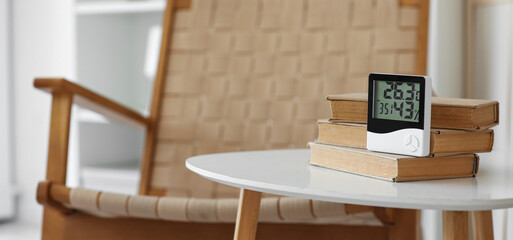Digital hygrometer with books on table in living room, closeup