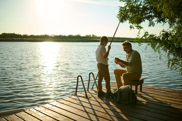 Grandfather and grandson fishing on pier at sunset having fun