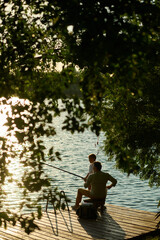 Grandfather and grandson fishing together on wooden dock at sunset