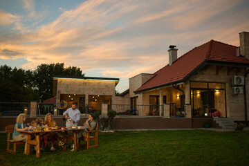 Family enjoying dinner together in backyard as sun sets behind house