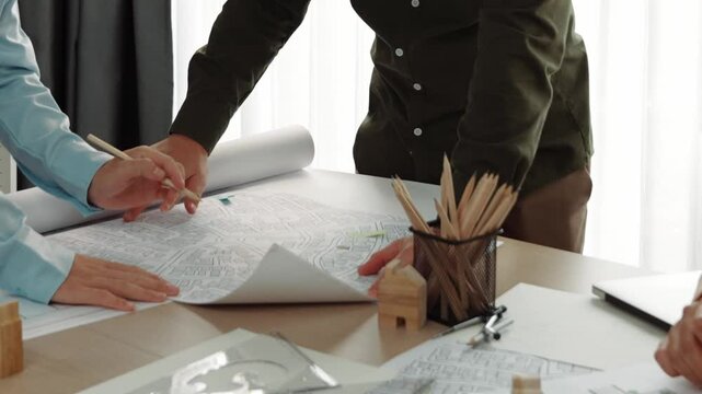 Smart architect and safety engineer discussion about building blueprint on table with architectural document, measurement tools and wooden block scatter around at modern office. Closeup. Delineation.
