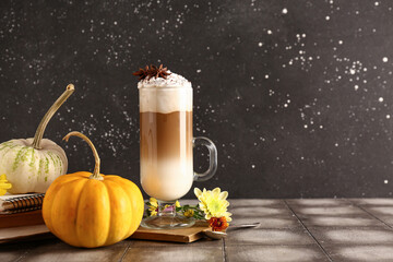 Glass cup of tasty pumpkin latte with star anise and beautiful flowers on grey tile table