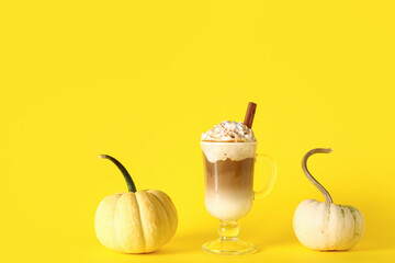 Glass cup of tasty pumpkin latte with cinnamon on yellow background