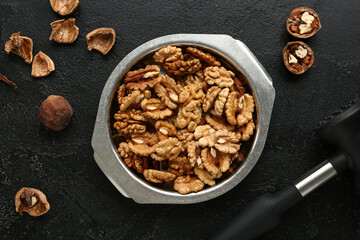 Metal bowl of tasty walnuts on black background