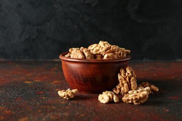 Bowl of tasty walnuts on table against black wall
