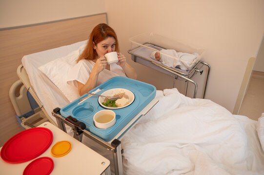 Caucasian woman eats on hospital bed after giving birth. 