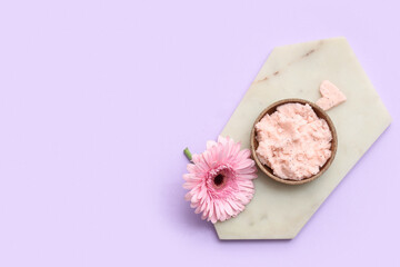 Board with bowl of natural body scrub and flower on lilac background