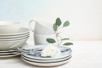 Beautiful tableware with flower and leaves on table near light wall
