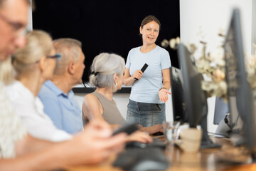 Middle-aged female instructor teaching computer skills to old students during IT classes