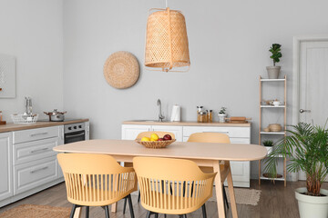 Interior of stylish kitchen with dining table, chairs, white counters and lamp