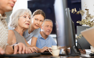 Old-aged female student learning computer programs with teacher in training room