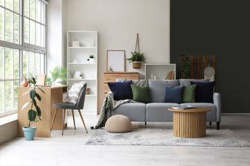 Coffee table, cozy sofa and table with chair near large window in living room