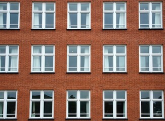 Fototapeta premium Front view of building with white windows, red brick wall in Copenhagen Denmark. Windows with curtains. Facade detail. Urban landscape. Cityscape pattern. Architecture background. Travel destination.